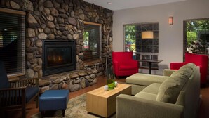 A living room with a stone wall, a fireplace, red and beige furniture, and large windows. - Country Inn & Suites by Radisson, Portland International Airport, OR (Portland)