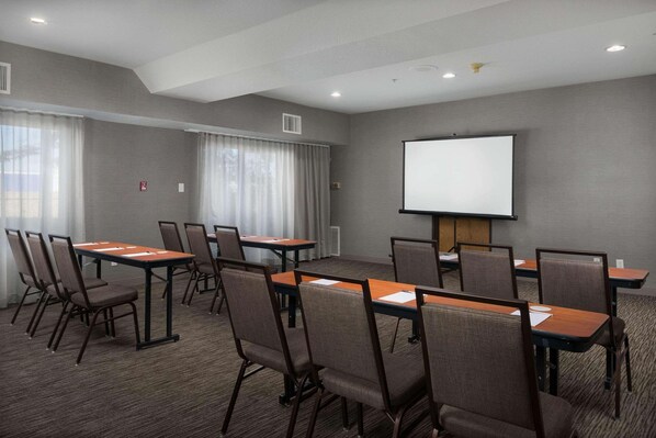 A conference room with a large screen, multiple tables, and chairs arranged for meetings.