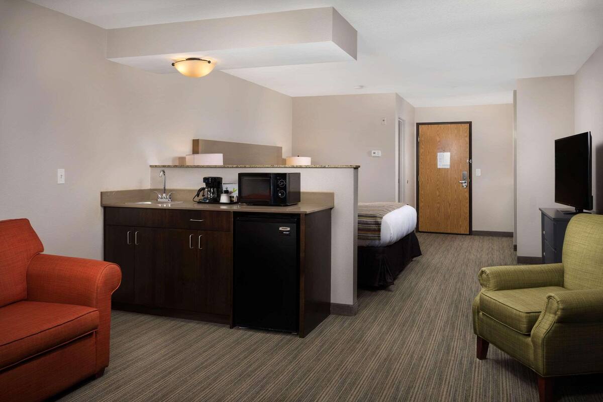 A compact hotel room with a kitchenette, a single bed, a sofa, and a television.