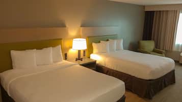 Een hotelkamer met twee bedden, een nachtkastje met een lamp, een stoel en een raam met gordijnen.