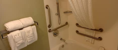 Un baño con bañera, barras de apoyo, cabezal de ducha y un perchero para toallas.