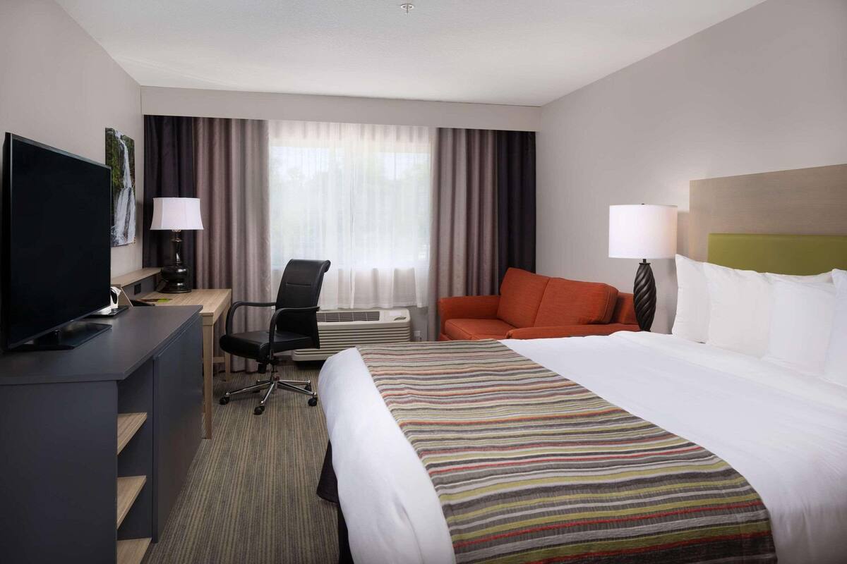 A hotel room with a bed, a desk with a computer, a chair, a television, and a window with curtains.