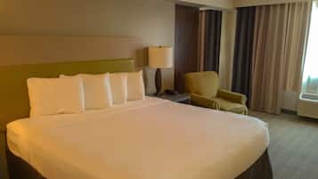 A hotel room with a large bed, a chair, a nightstand, a lamp, and a window with curtains.