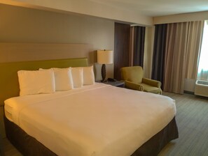 A hotel room with a large bed, a chair, a nightstand, a lamp, and a window with curtains.