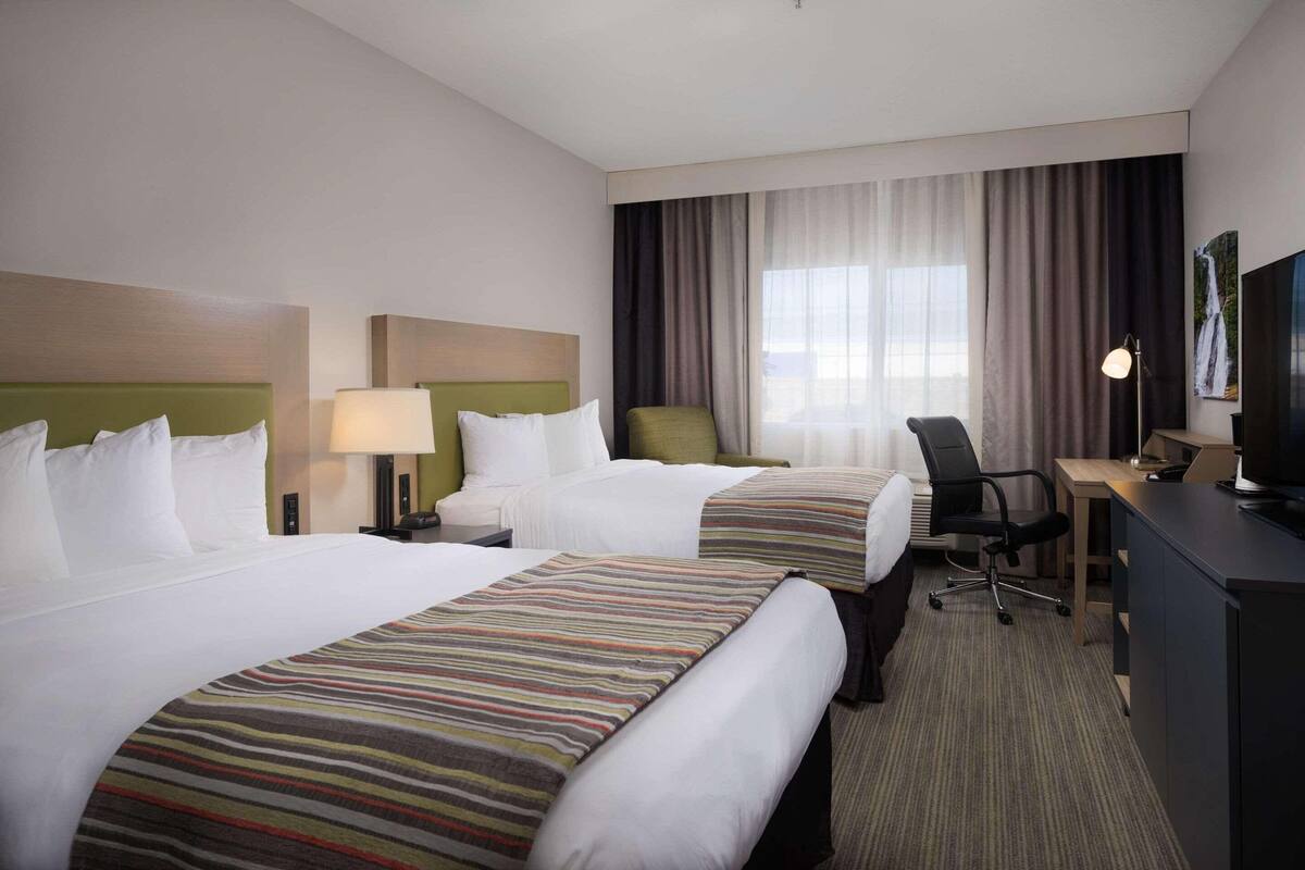 A hotel room with two beds, a desk, a chair, a TV, and a window with curtains.