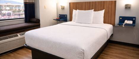 A hotel room with a large bed, a window with a view, a bedside table with a phone, and a wall-mounted heater.