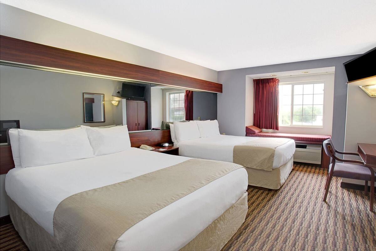 A hotel room with two beds, a desk, a chair, a TV, and a window with curtains.