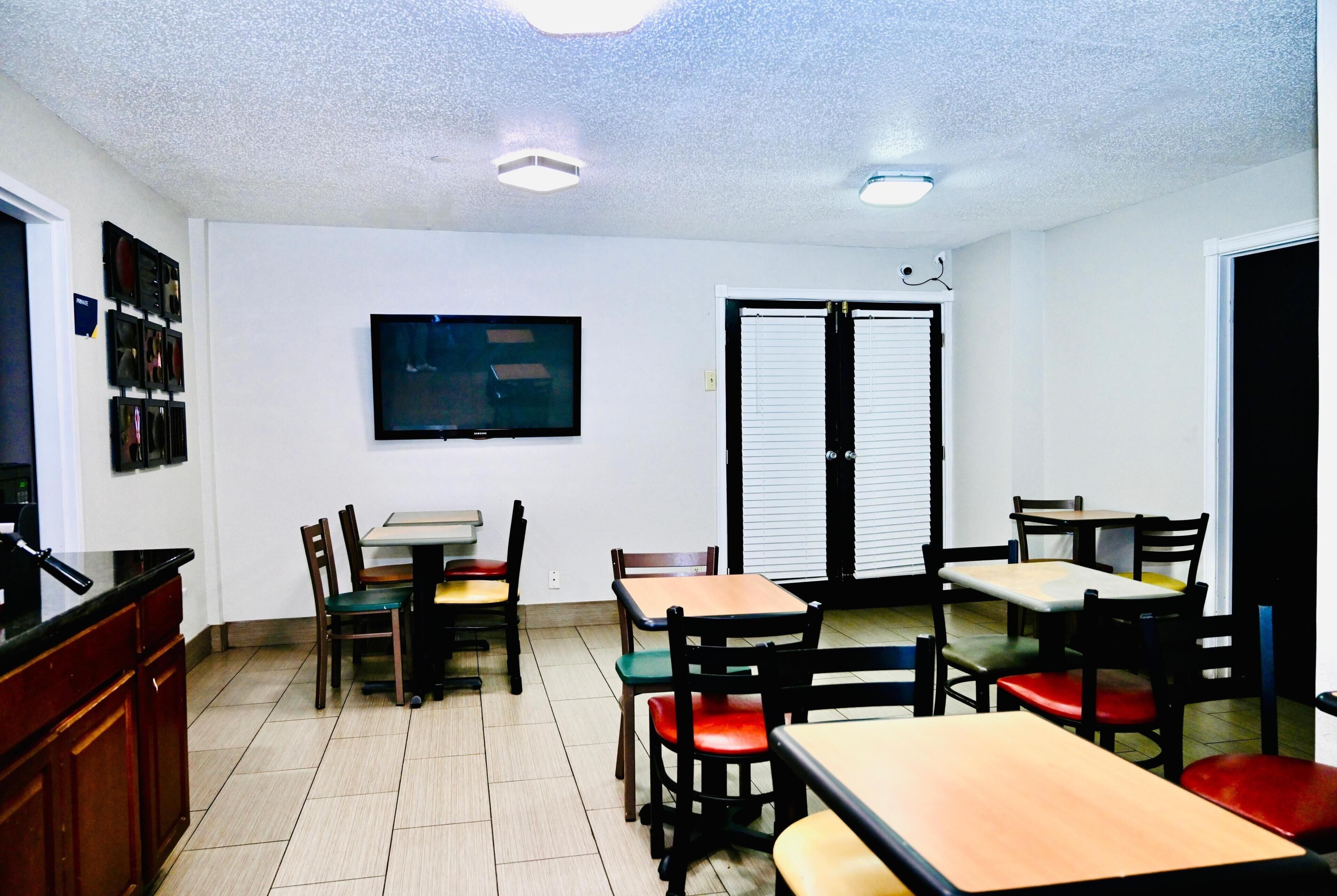 A room with a TV, multiple tables and chairs, a door, and a ceiling light.