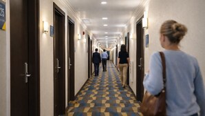 Un pasillo de hotel con piso a cuadros, puertas a ambos lados e iluminación en el techo.