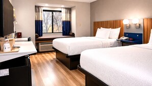 Habitación de hotel con dos camas, un escritorio con computadora, una ventana con cortinas y una mesita de noche con teléfono.