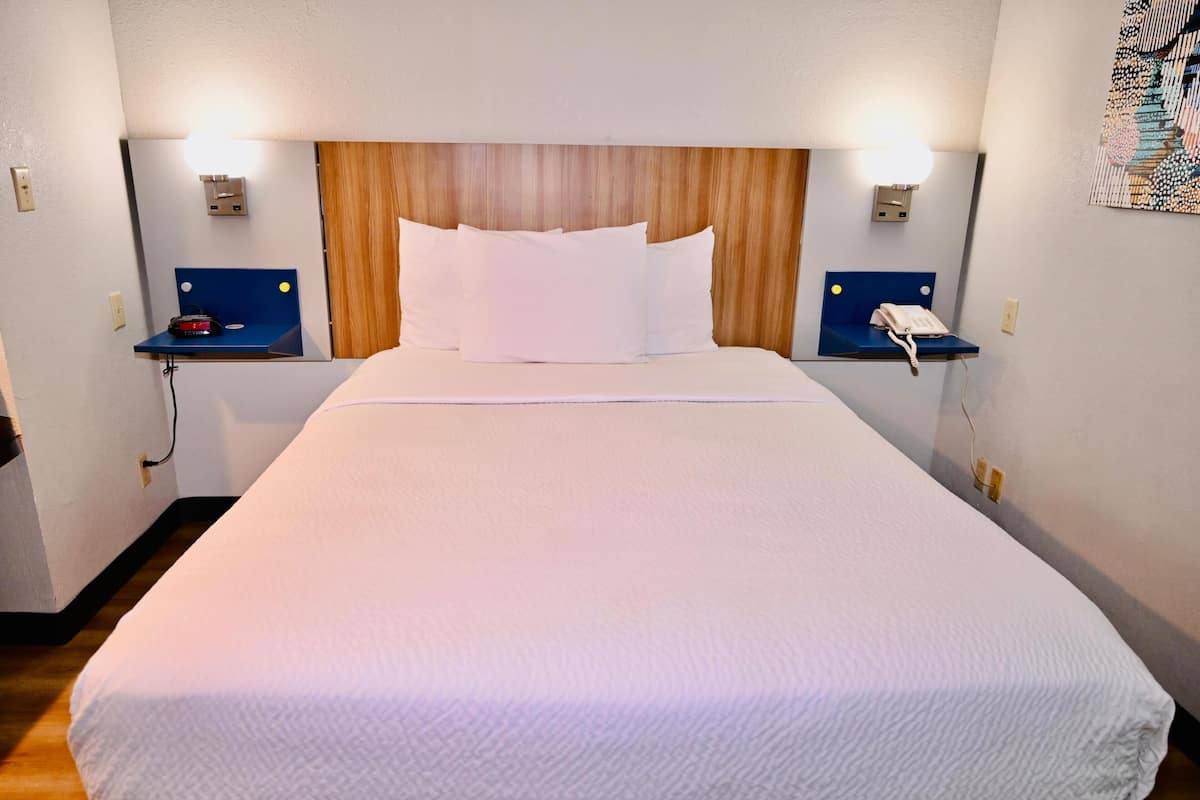 A hotel room with a wooden headboard, white bedding, two bedside tables with lamps, and a telephone.