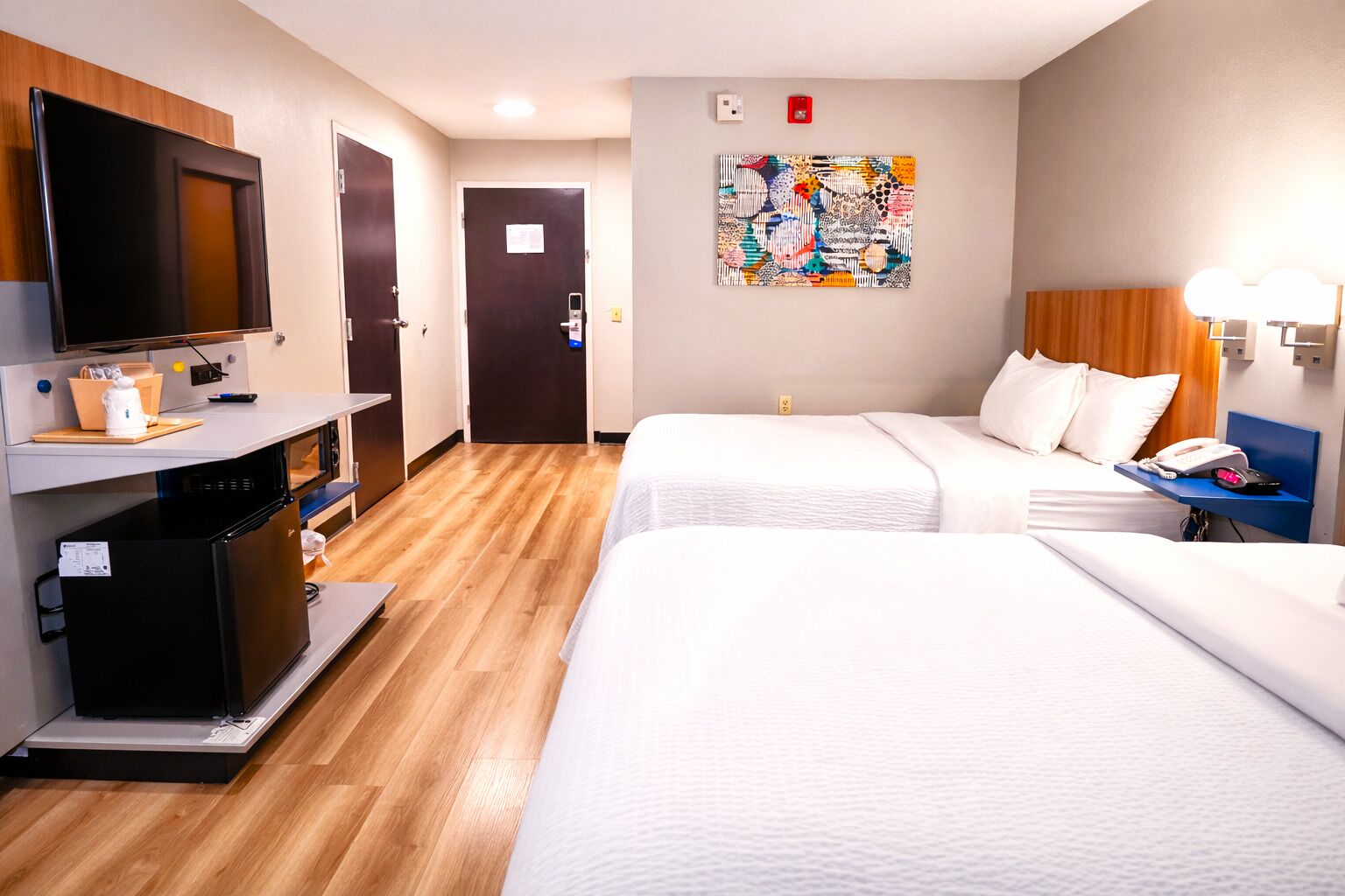 Une chambre d’hôtel avec deux lits, une télévision, un réfrigérateur, un bureau et un tableau au mur.