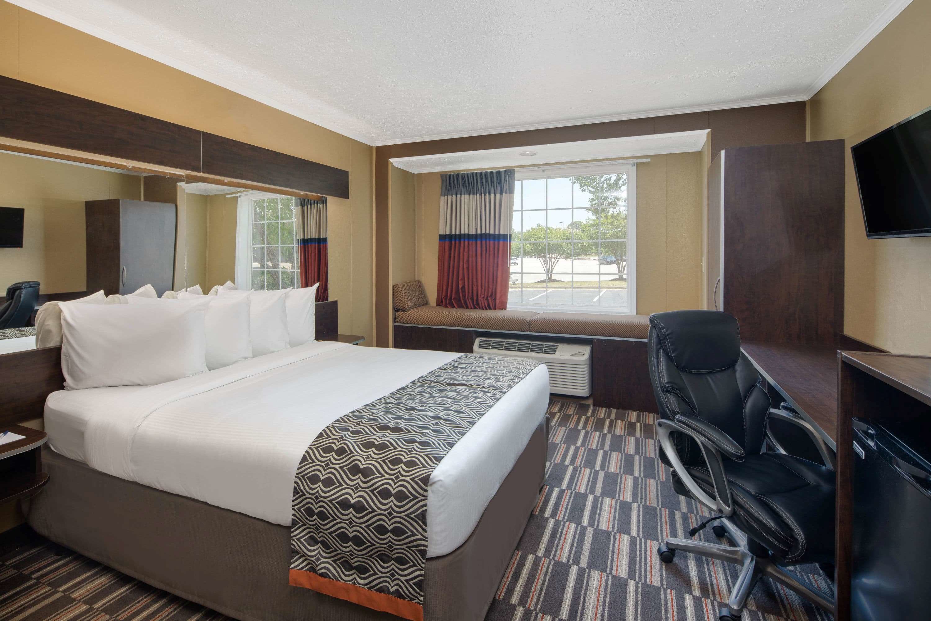 Habitación de hotel con una cama grande, un escritorio con silla, televisión y ventana con cortinas.