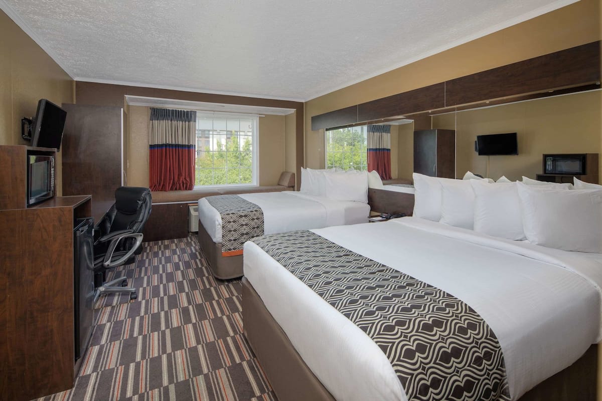 A hotel room with two beds, a desk with a chair, a television, and a window with curtains.