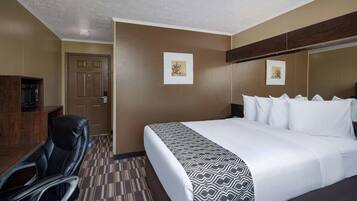 A hotel room with a bed, a desk, and a chair. There are two framed pictures on the wall.