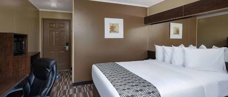 A hotel room with a bed, a desk, and a chair. There are two framed pictures on the wall.