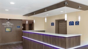 A reception desk with a wooden finish and purple underlighting, a sign for the Microtel Inn by Wyndham, and a door with a sign indicating check-in times and no pets allowed. - Microtel Inn & Suites by Wyndham Columbia/Fort Jackson N (Columbia)