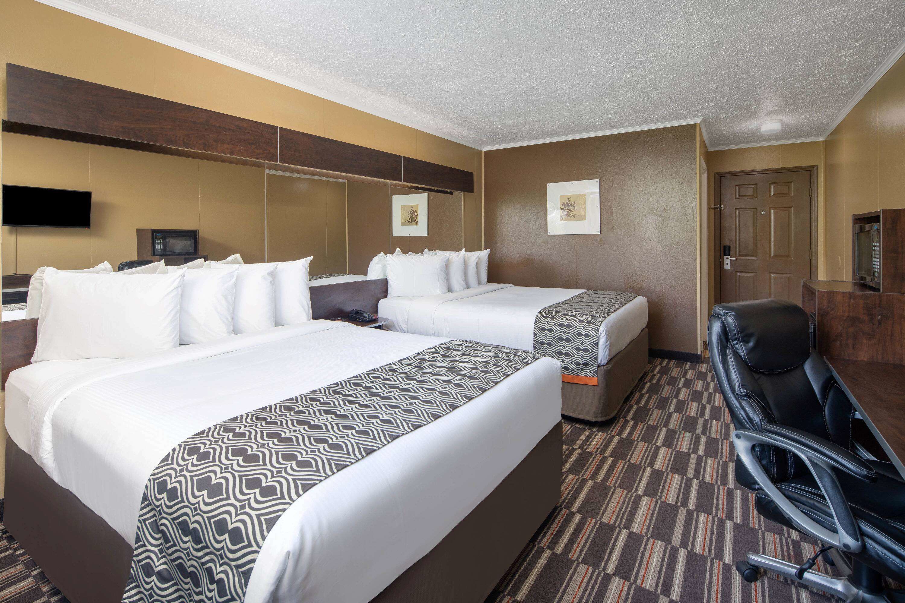 Une chambre d’hôtel avec deux lits, un bureau, une chaise, un téléviseur à écran plat et une porte.