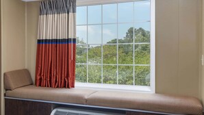 A window seat with a checkered cushion, a window with a grid pattern, and a view of greenery outside. - Microtel Inn & Suites by Wyndham Columbia/Fort Jackson N (Columbia)