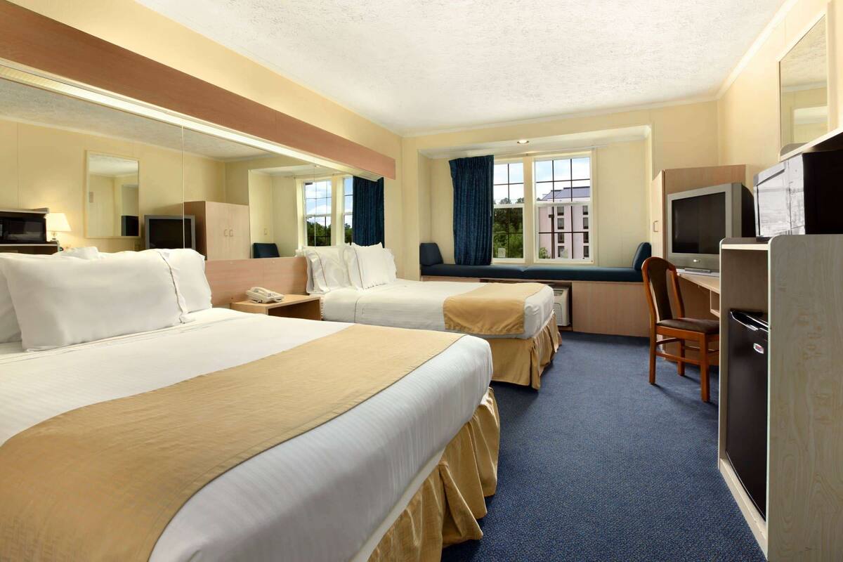 A hotel room with two beds, a desk, a chair, a television, and a refrigerator.