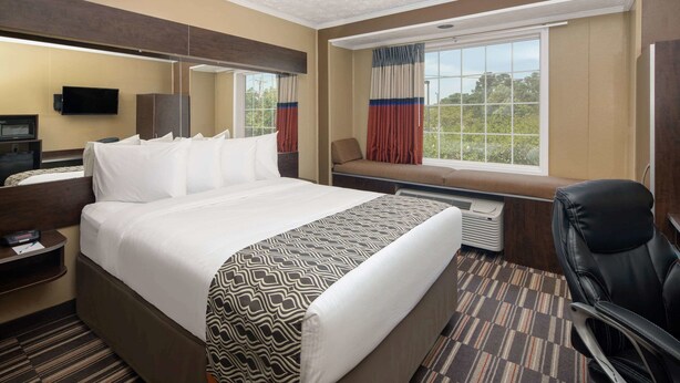A hotel room with a large bed, a desk with a computer, a chair, a window with curtains, and a view of greenery outside. - Microtel Inn & Suites by Wyndham Columbia/Fort Jackson N (Columbia)