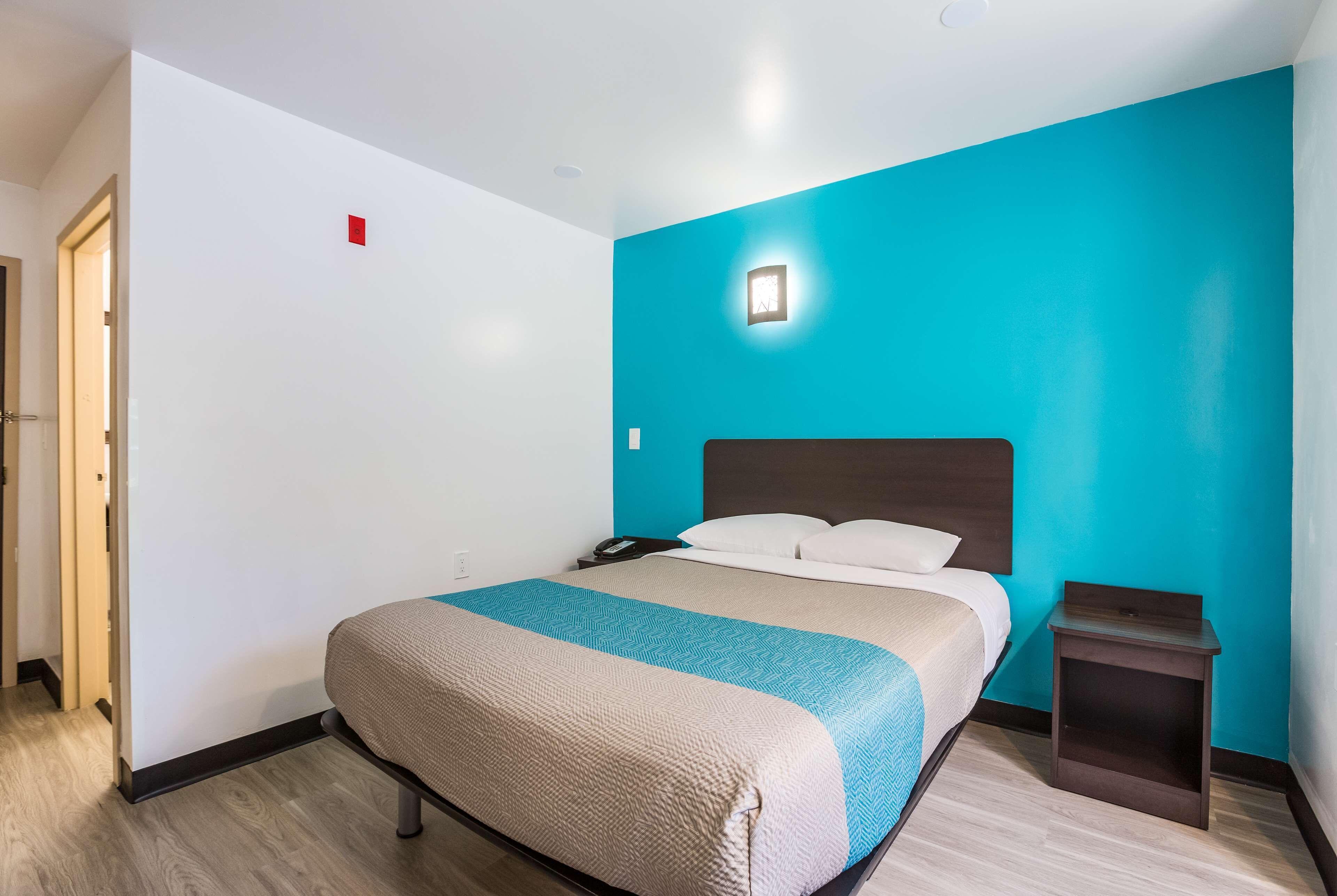 A hotel room with a bed, a nightstand, a wall-mounted phone, and a door.