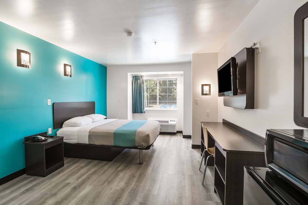 A modern hotel room with a bed, a desk, a TV, and a window with curtains.