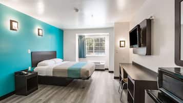 A modern hotel room with a bed, a desk, a TV, and a window with curtains.
