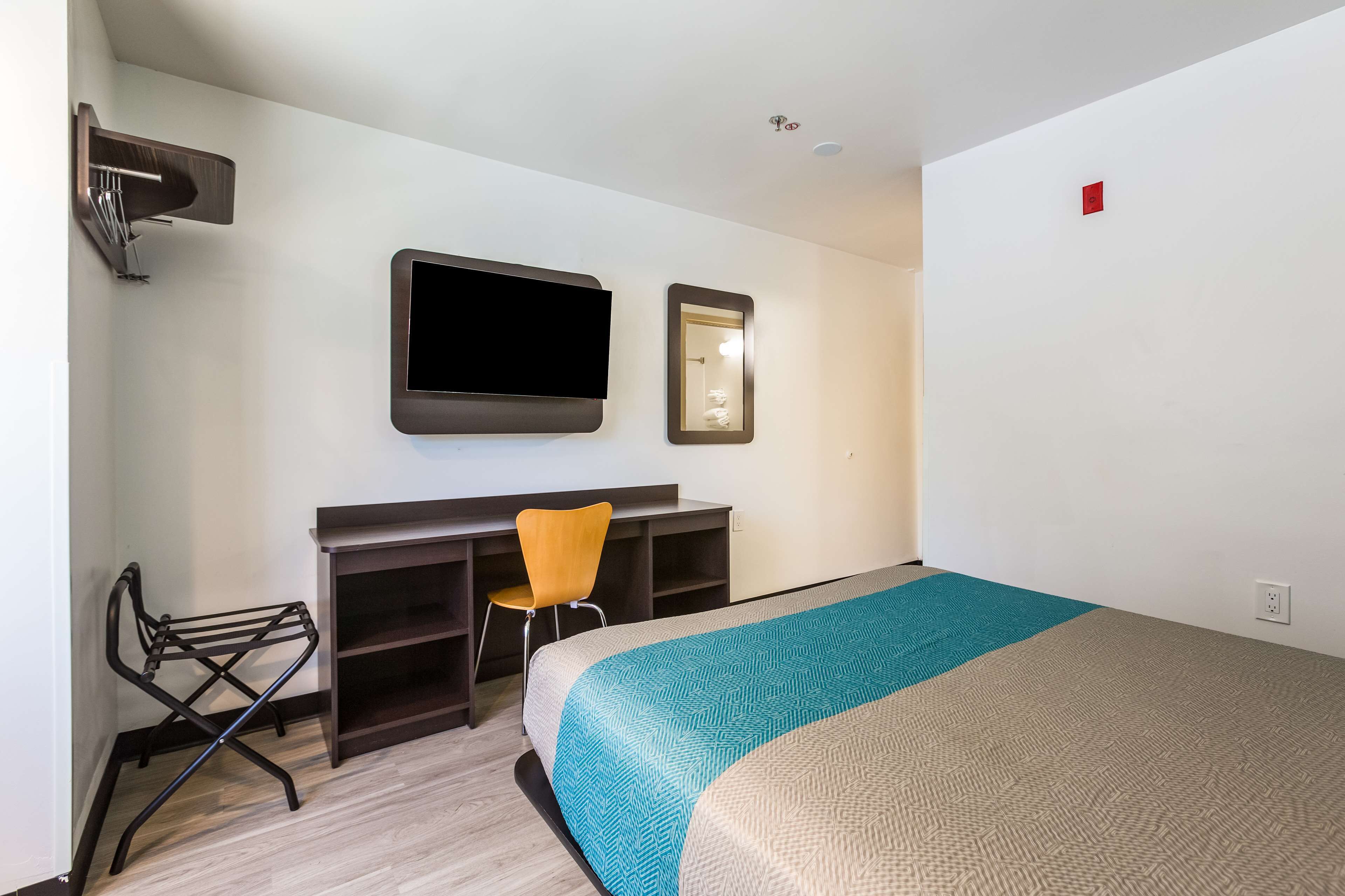 A hotel room with a bed, a desk, a chair, a TV, and a mirror.