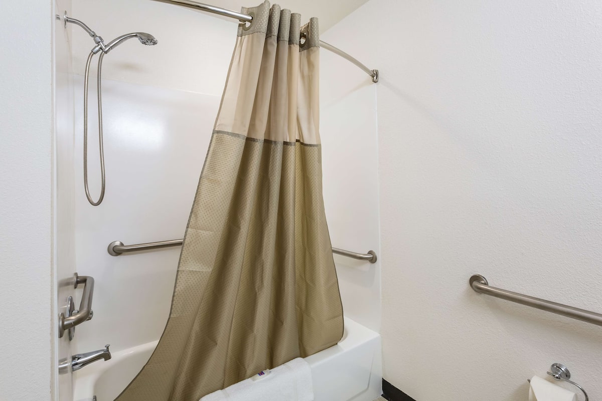 A bathroom with a shower curtain, grab bars, a towel rack, and a toilet paper holder.