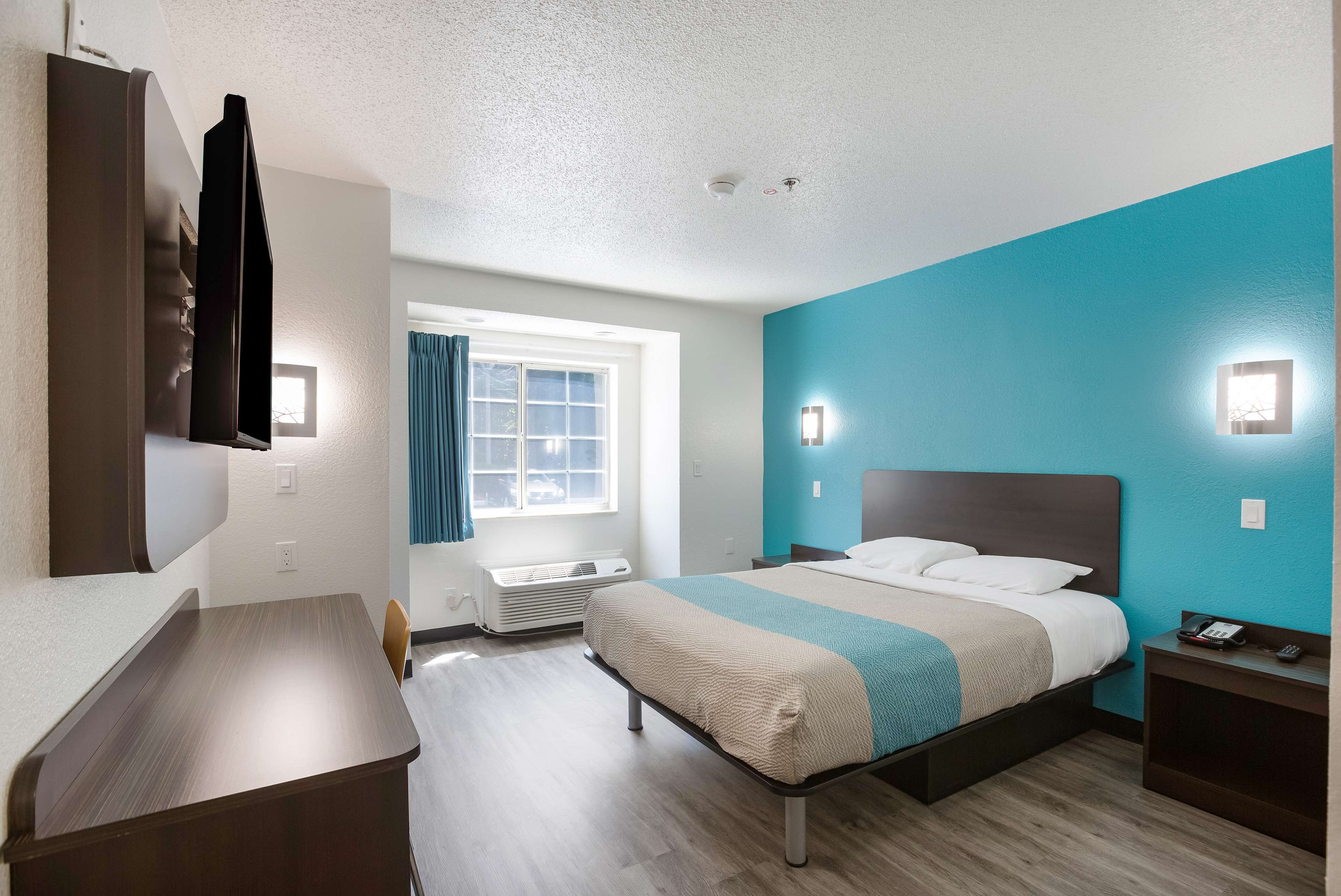 A hotel room with a bed, bedside table, and a desk.