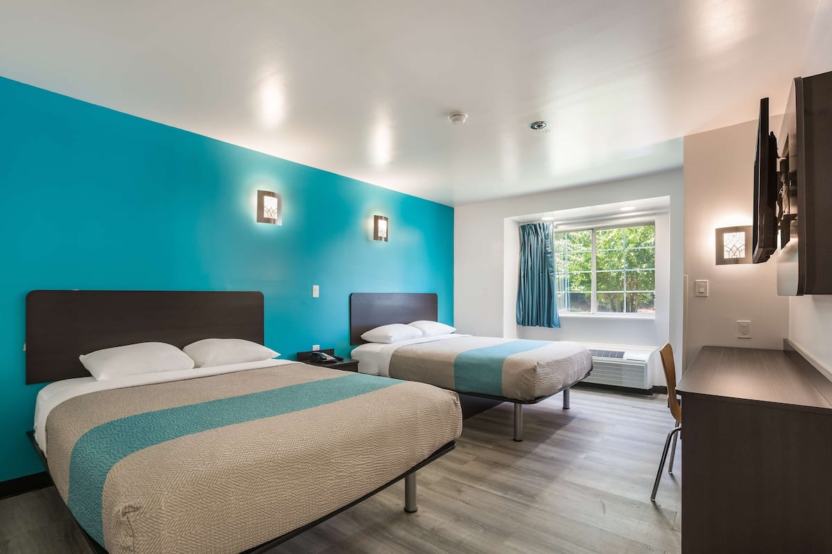 A hotel room with two beds, a desk, and a window with curtains.