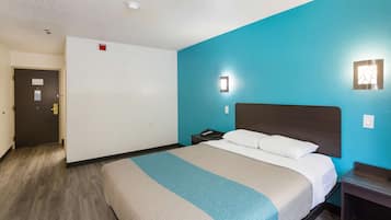 Una habitación de hotel con una cama, una mesita de noche, una lámpara fijada a la pared y una puerta.