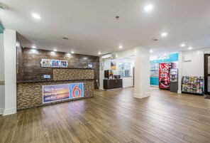 Zona de recepción de un hotel con un mostrador de madera, una pantalla digital y una máquina expendedora.