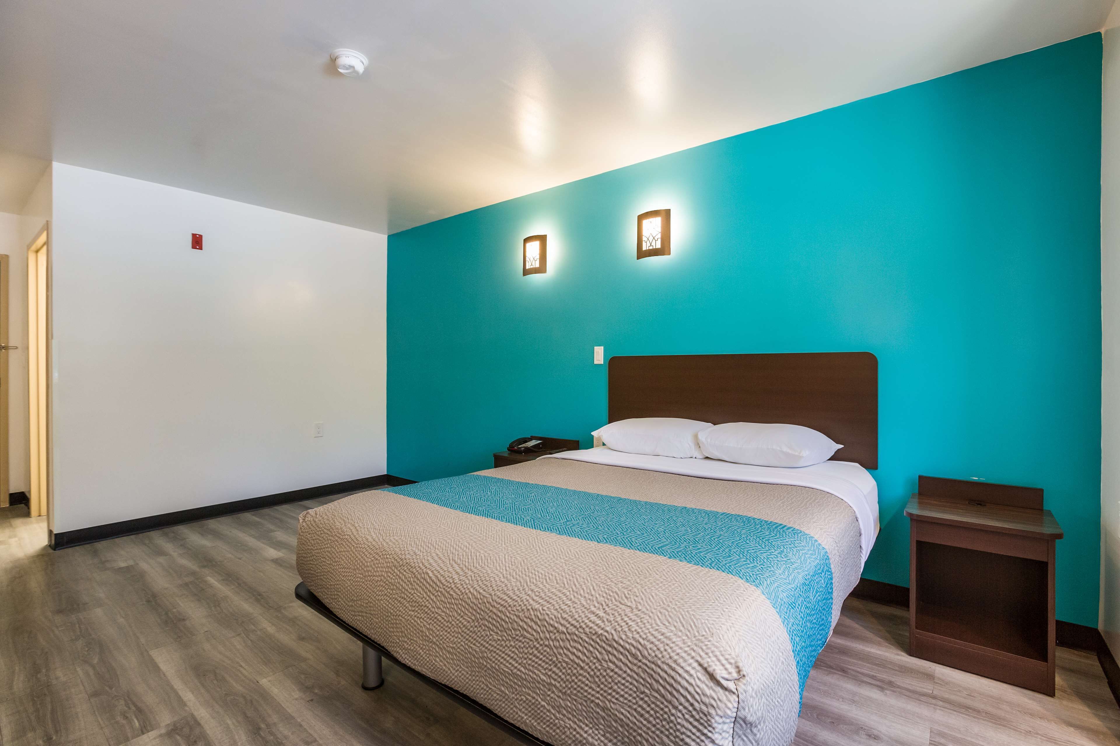 A hotel room with a large bed, a wooden headboard, a nightstand, and a teal accent wall.