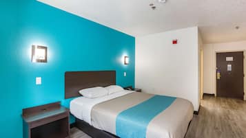 Una habitación de hotel con una cama, una mesita de noche, una lámpara de pared y una puerta.