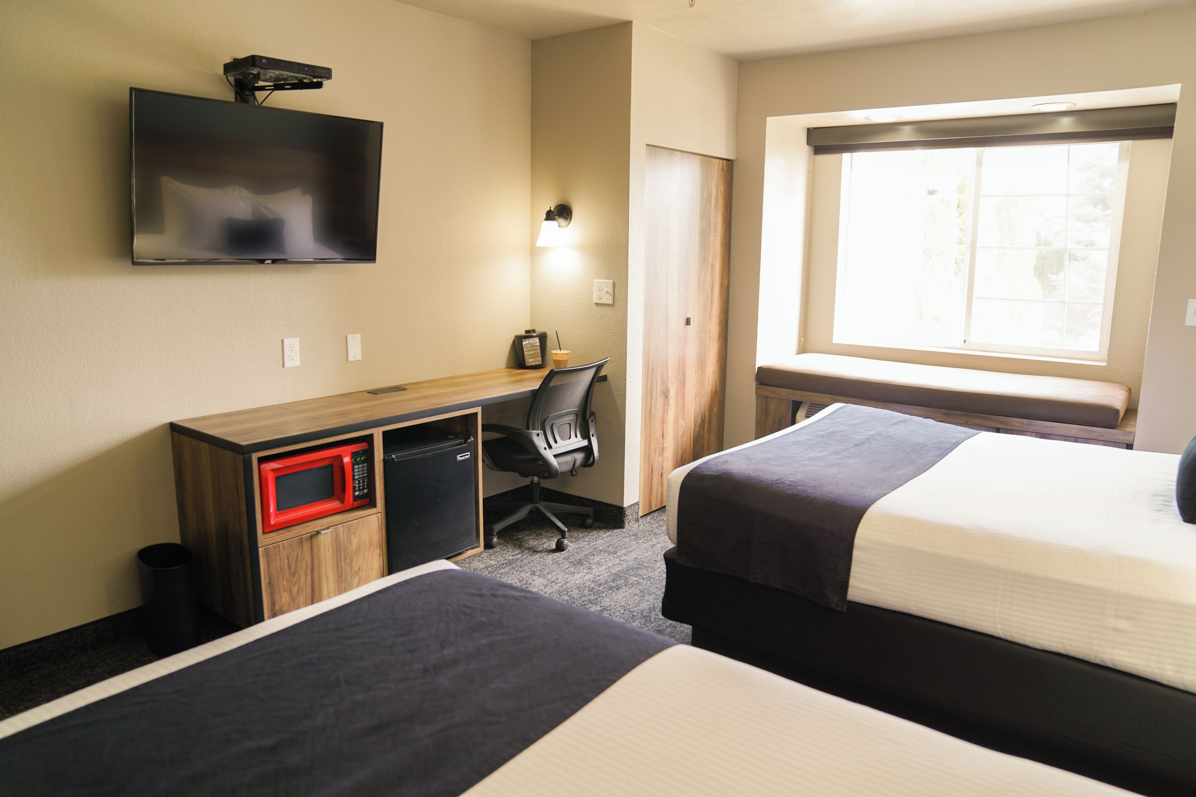 Une chambre d’hôtel avec deux lits, un bureau équipé d’un micro-ondes, une télévision et une fenêtre donnant sur un paysage agréable.