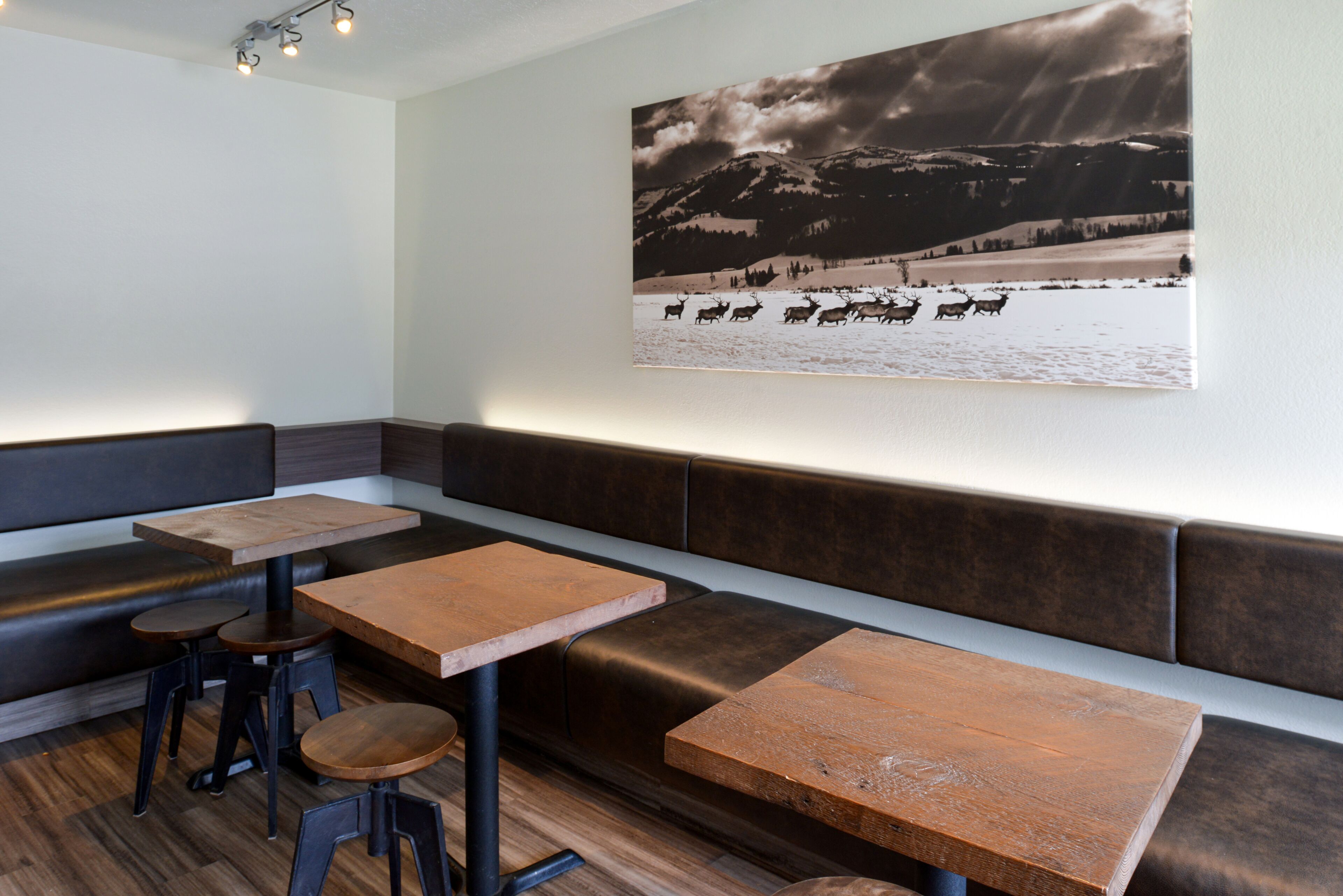 A restaurant interior with wooden tables and benches, a large wall-mounted picture of a snowy landscape, and a wooden floor.