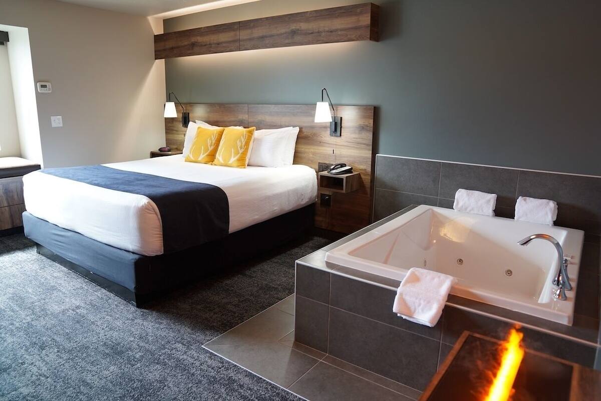 A modern hotel room with a large bed, a separate bathroom with a bathtub, and a small bedside table with a lamp.