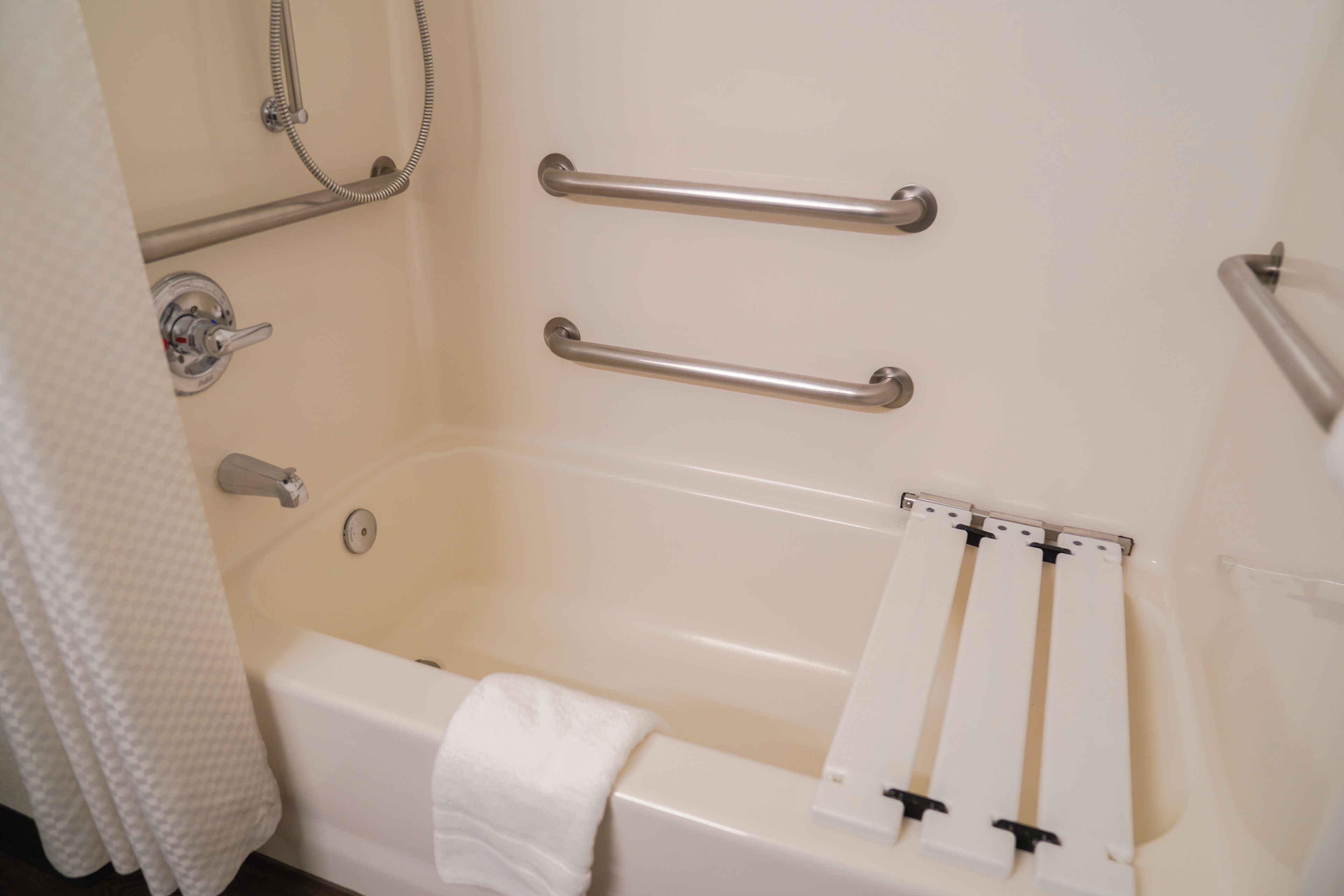 Un baño con bañera, barras de apoyo, cabezal de ducha y un perchero para toallas.