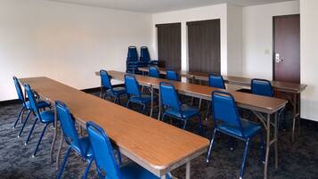 A conference room with long tables and blue chairs, carpeted floor, and a door in the background.