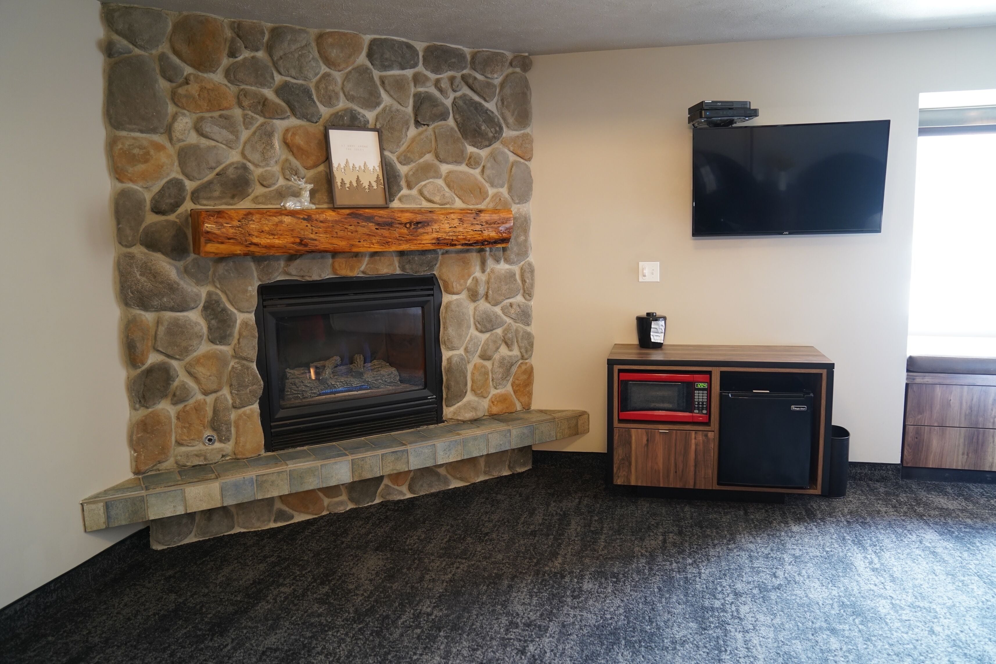 A stone fireplace with a wooden mantel, a flat-screen TV mounted on the wall, and a built-in microwave and refrigerator unit.