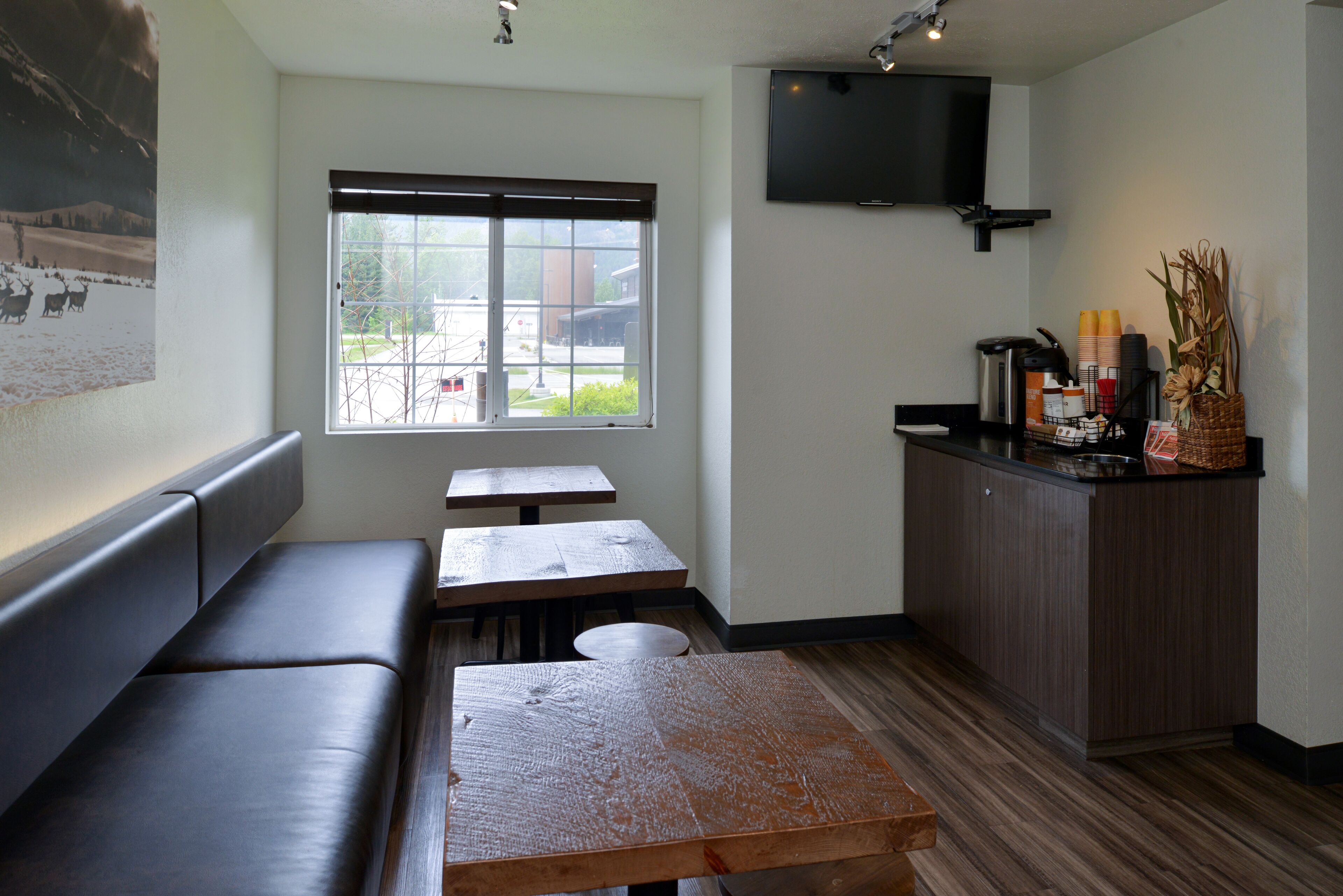 A restaurant with a long counter, a television mounted on the wall, and a window with a view of the outside.