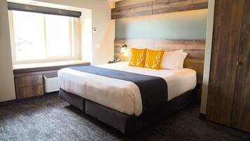 Een moderne hotelkamer met een groot bed, een raam met luxaflex, een nachtkastje met een lamp en een garderobe.