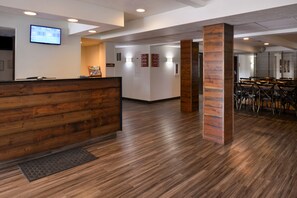 A reception area with a wooden reception desk, a digital screen, and a seating area with tables and chairs.