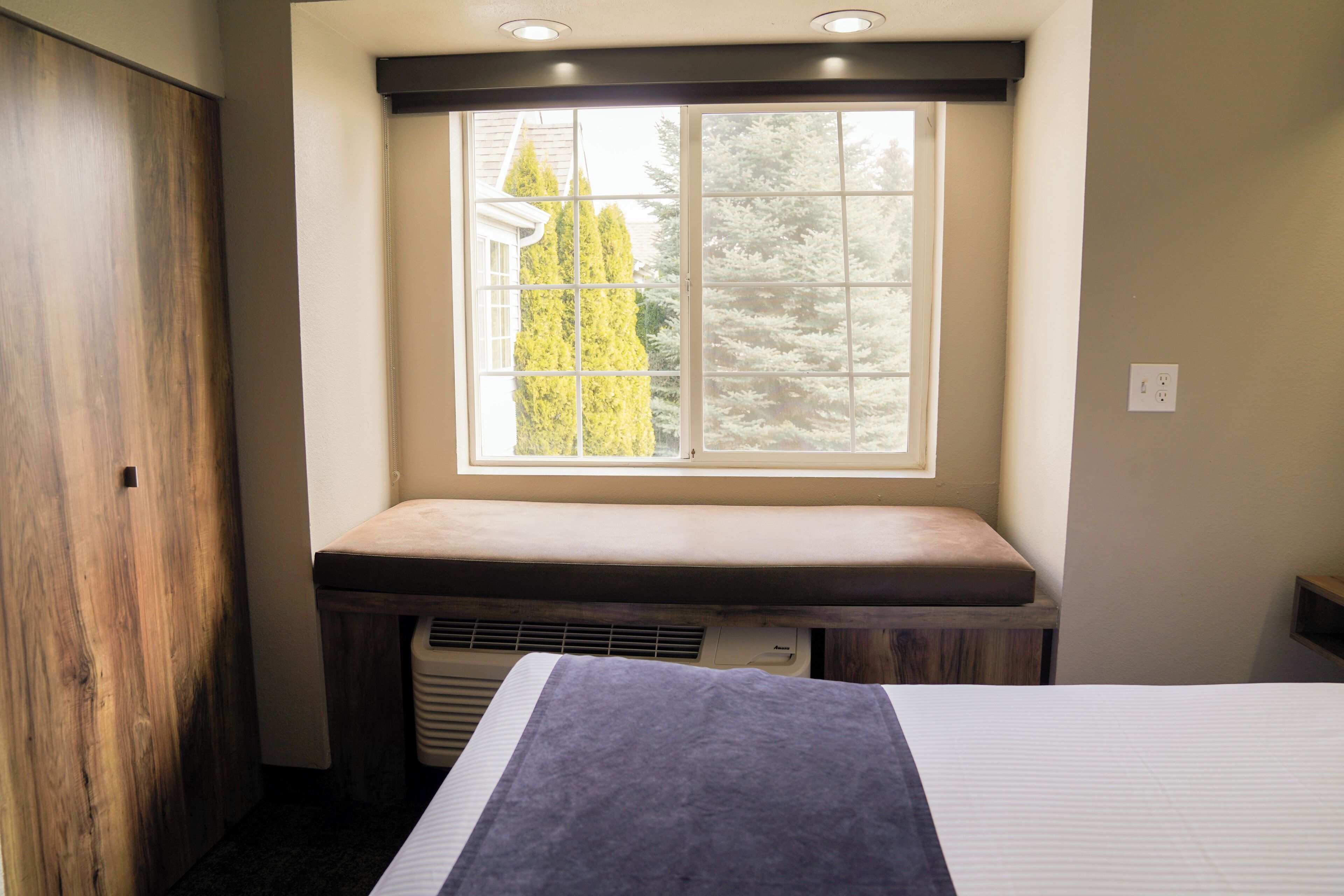 A bedroom with a window, a bed, a bench, and a wardrobe.