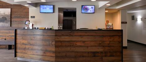 A reception desk with wooden paneling, two monitors, and a digital screen displaying information.