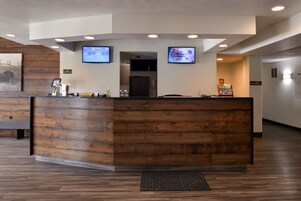 Un mostrador de recepción con paneles de madera, dos monitores y una pantalla digital que muestra información.