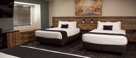 A hotel room with two beds, a TV, a painting, and a window with blinds.