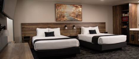 A hotel room with two beds, a painting on the wall, a wooden headboard, a desk, and a cabinet with a microwave.